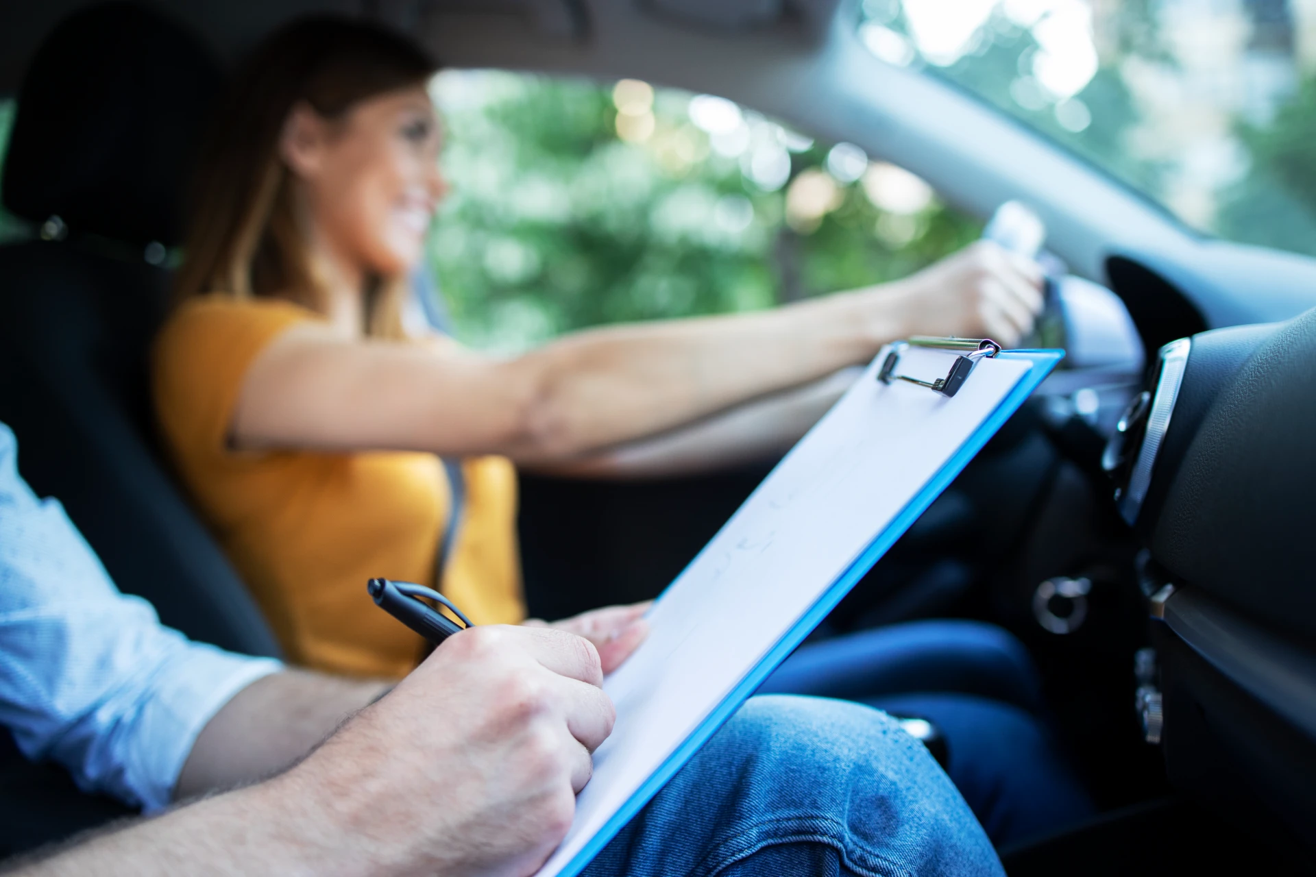 close up view driving instructor holding checklist while background female student steering driving car
